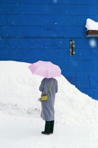 person standing in the snow against a blue wall with pink umbrella